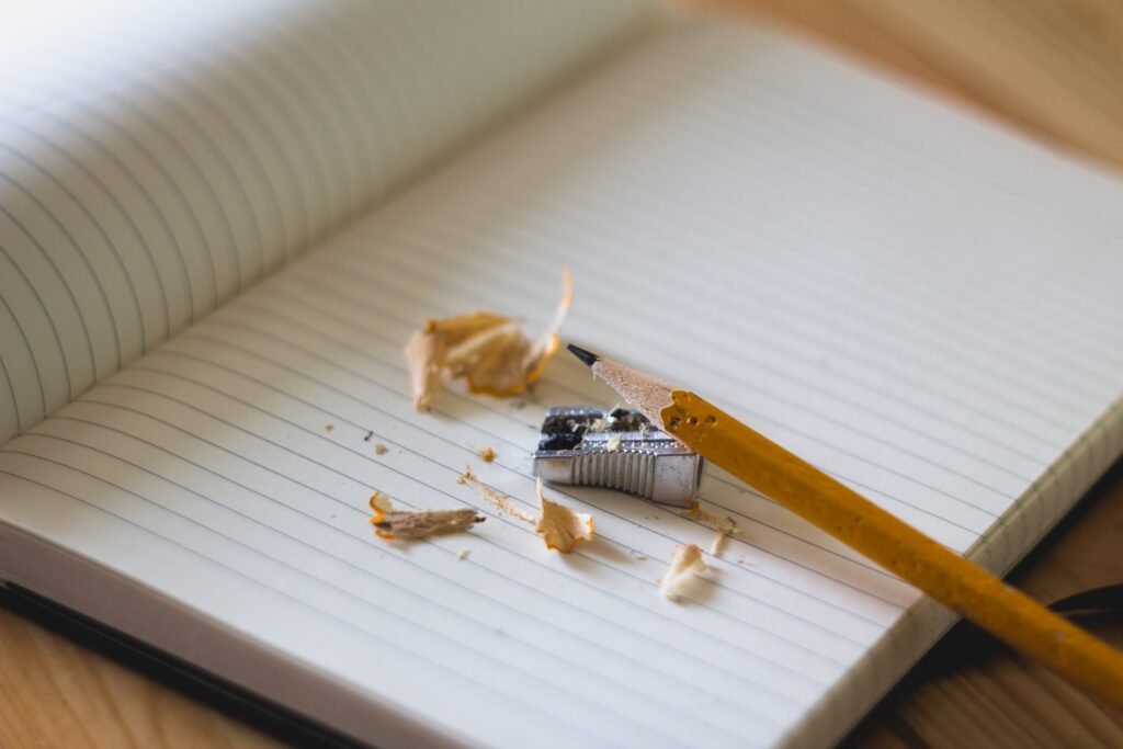 Pencil and pencil shavings, open blank notebook and pencil sharpner.