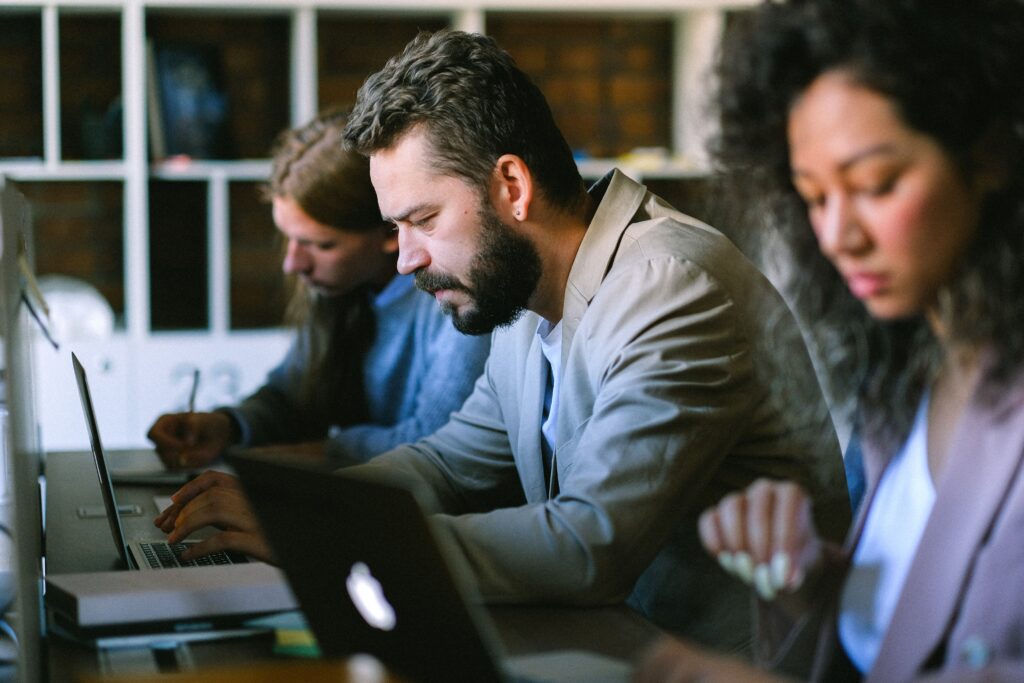 Three employees, seated at a table working on laptops.