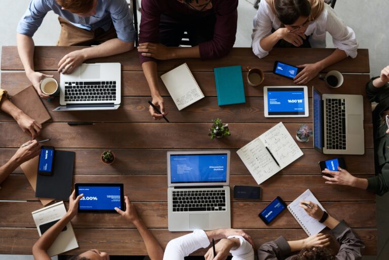 Overhead view, people working with laptops and notebooks at a wooden table.